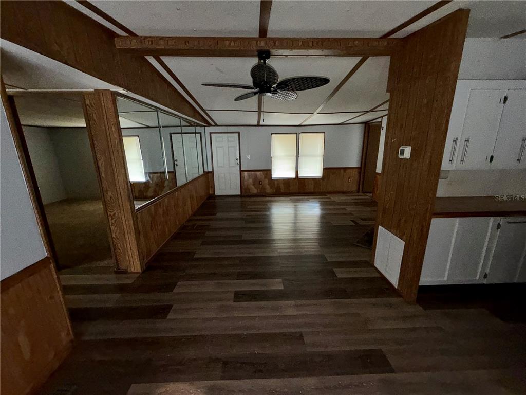 An interior view of a living area featuring wood-paneled walls, wood-look flooring, and a ceiling fan — 34321 COUNTRYSIDE DRIVE, WESLEY CHAPEL, FL