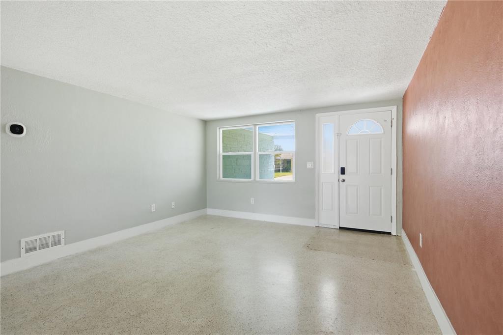 An empty room features light gray walls, a terracotta accent wall, and terrazzo flooring — 2051 PEGGY DRIVE, HOLIDAY, FL