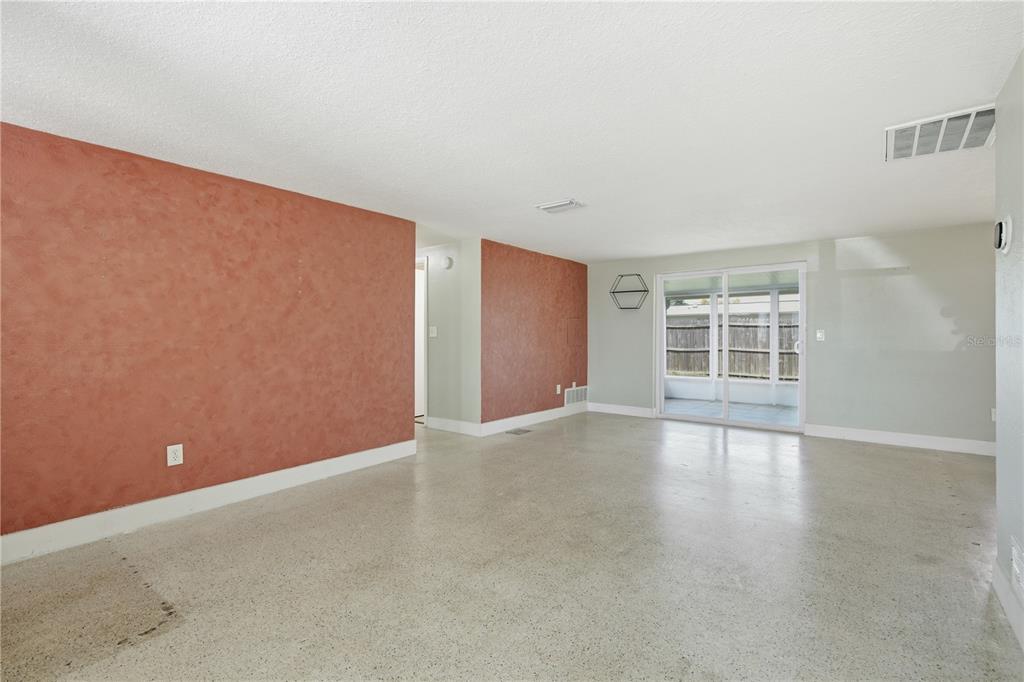 A living room features terracotta-colored accent walls, light-colored walls, and a polished concrete floor — 2051 PEGGY DRIVE, HOLIDAY, FL