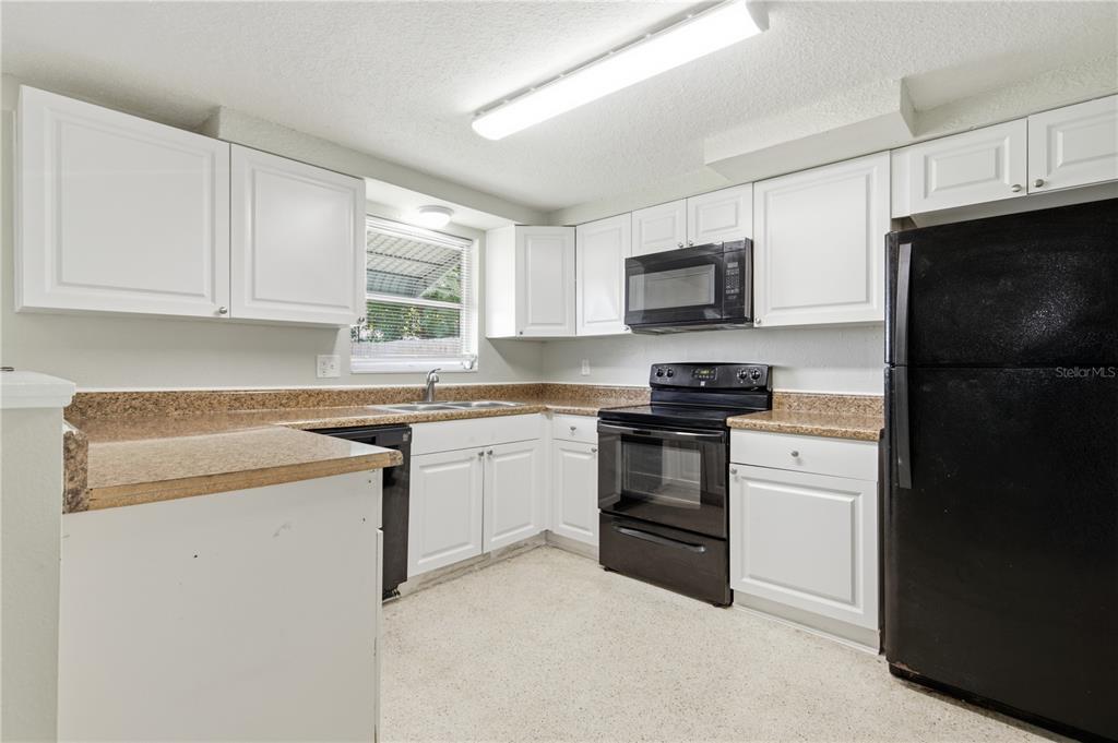 A kitchen with white cabinets, speckled countertops, and black appliances under a fluorescent light fixture — 2051 PEGGY DRIVE, HOLIDAY, FL