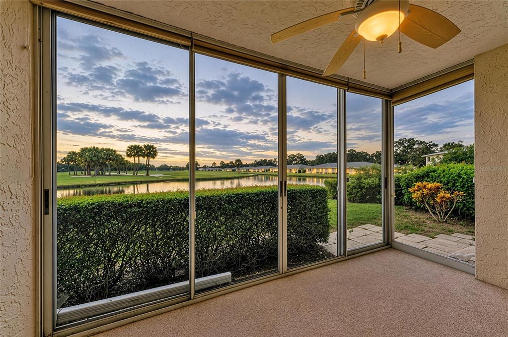 A carpeted sunroom with sliding glass doors overlooking a pond, golf course, and sunset sky — 6999 W COUNTRY CLUB DRIVE N UNIT 123, SARASOTA, FL