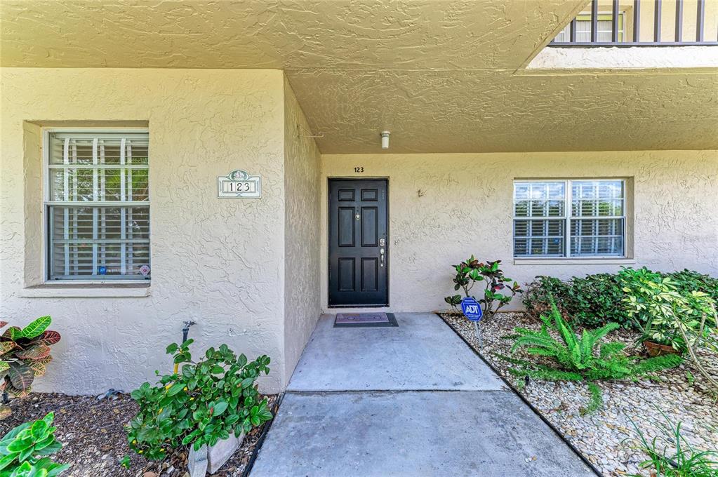 The exterior view shows a beige stucco building entrance with a black front door — 6999 W COUNTRY CLUB DRIVE N UNIT 123, SARASOTA, FL
