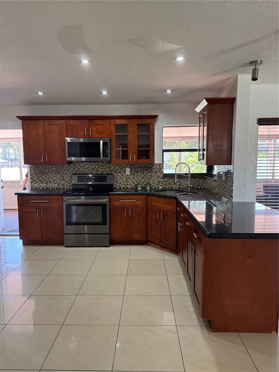A kitchen features cherry wood cabinets, stainless steel appliances, dark countertops, and light tile flooring — 8240 NW 181st St # 1, Hialeah FL 33015, HIALEAH, FL