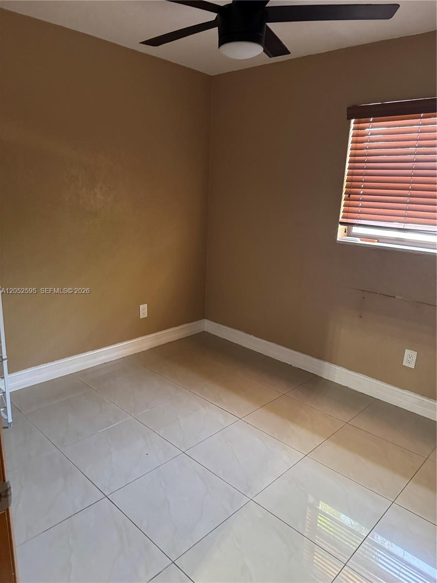 A bedroom with tan walls, light-colored tile flooring, a ceiling fan, and a window with blinds — 8240 NW 181st St # 1, Hialeah FL 33015, HIALEAH, FL