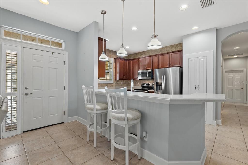 A kitchen features a breakfast bar with two white chairs, dark cabinetry, and tile flooring — 395 CAPULET DRIVE, VENICE, FL