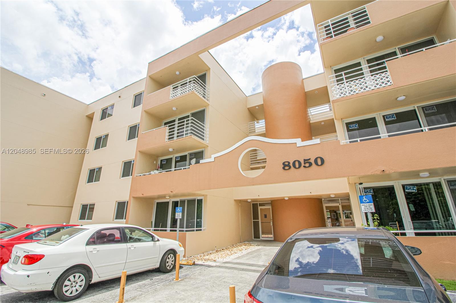 The exterior of a multi-story apartment building features a tan facade and a parking area — 8050 NW 8th St # 1306, Miami FL 33126, MIAMI, FL