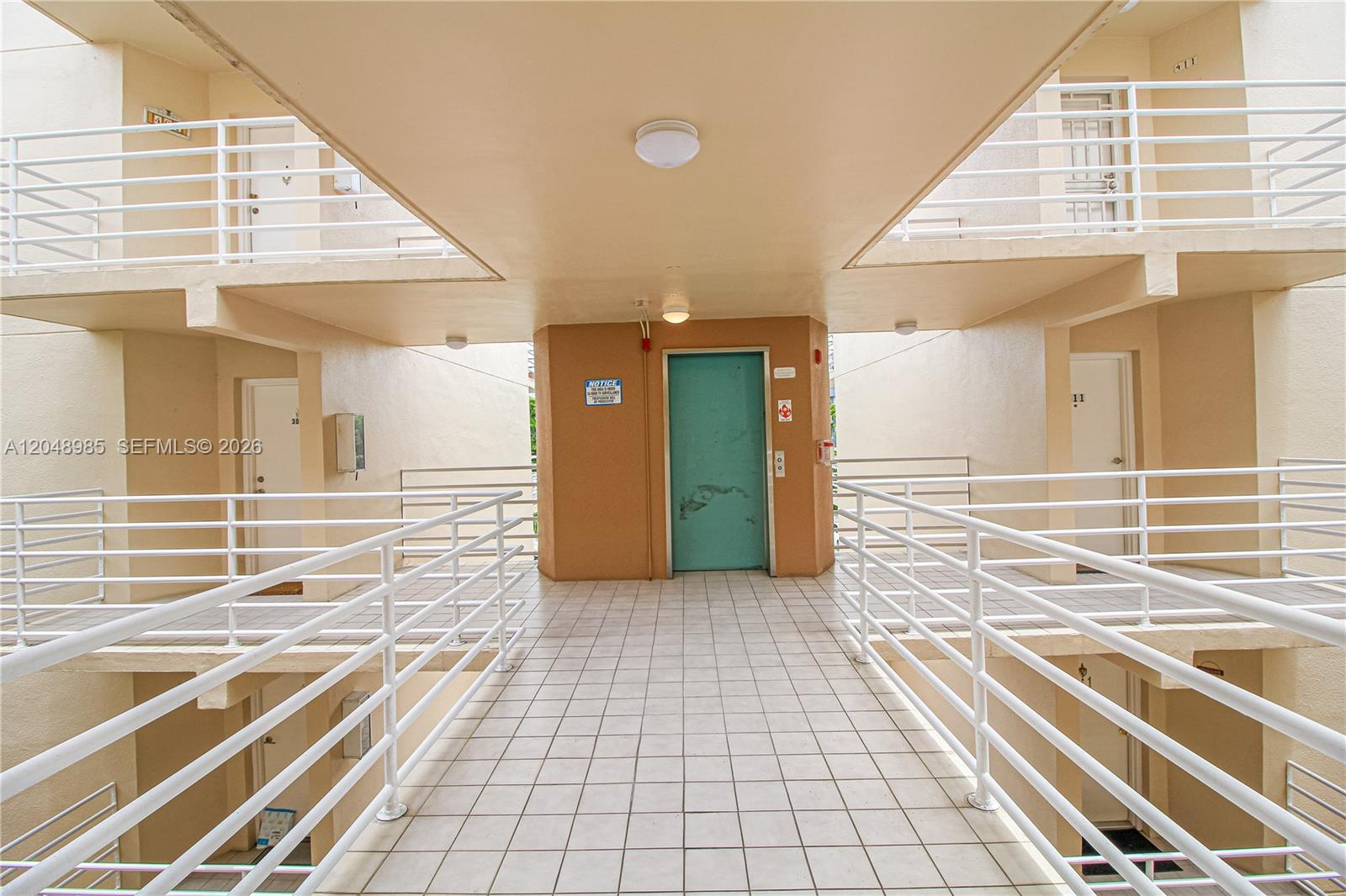 An outdoor apartment building walkway features tiled flooring, white railings, and a central elevator door — 8050 NW 8th St # 1306, Miami FL 33126, MIAMI, FL