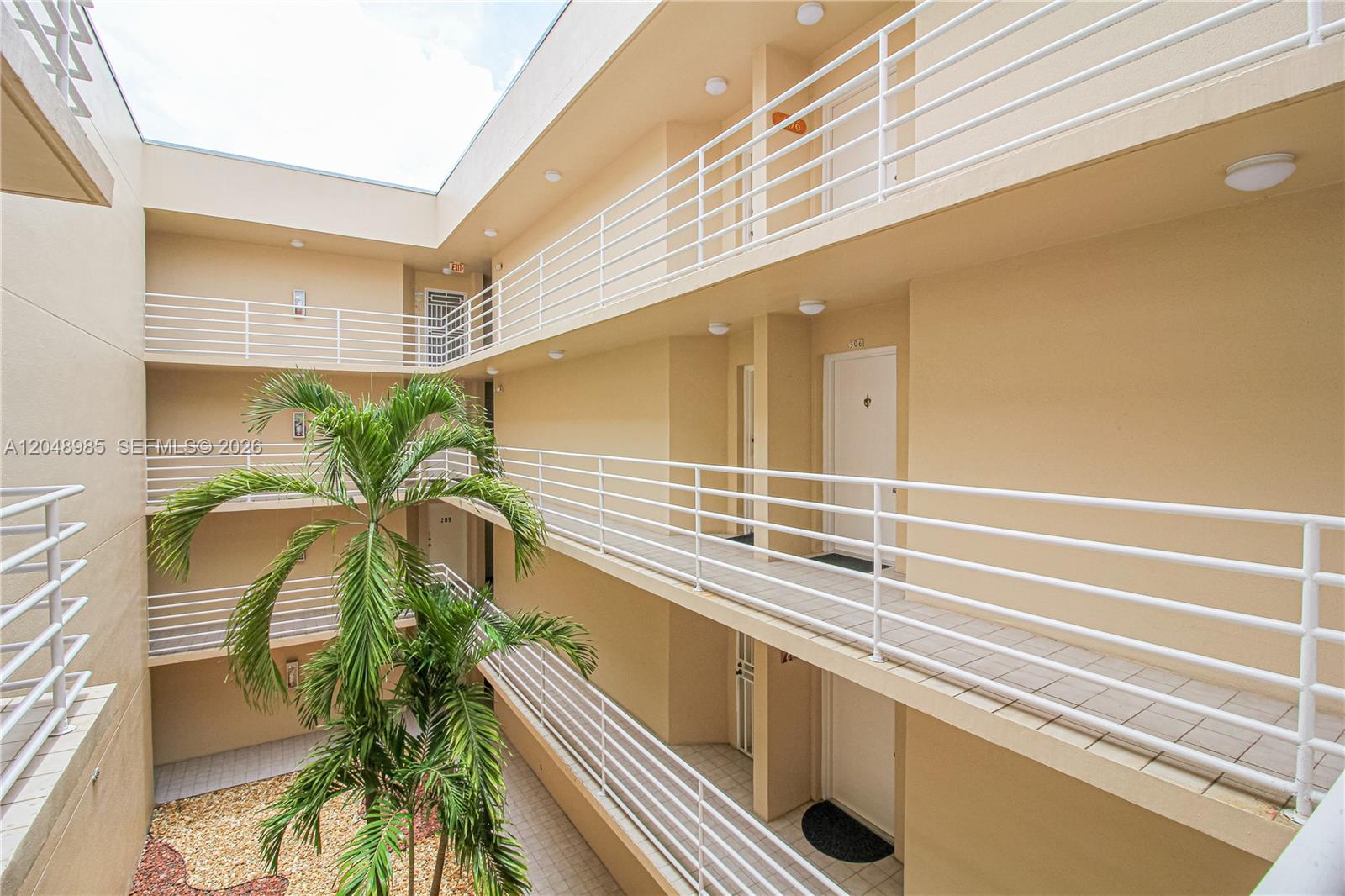 An open-air apartment building courtyard features tiered walkways with white railings and a palm tree — 8050 NW 8th St # 1306, Miami FL 33126, MIAMI, FL