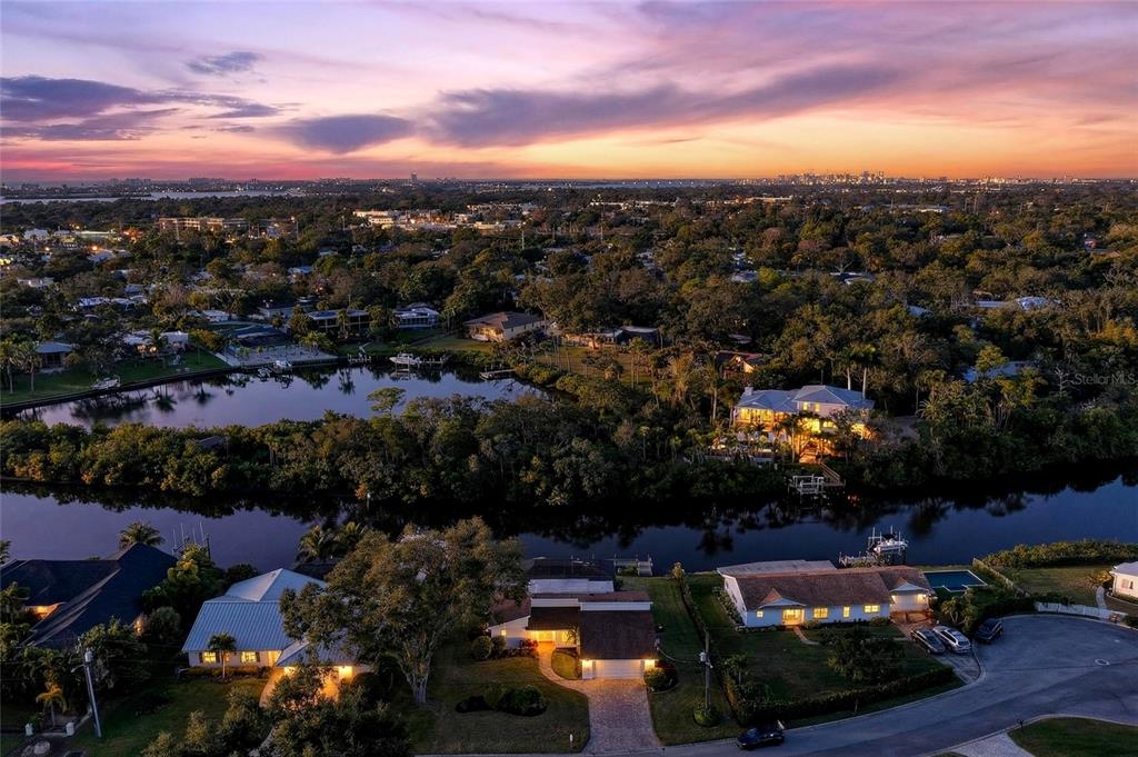 An aerial view shows waterfront homes surrounded by trees under a colorful sunset sky — 5424 AMERICA DRIVE, SARASOTA, FL