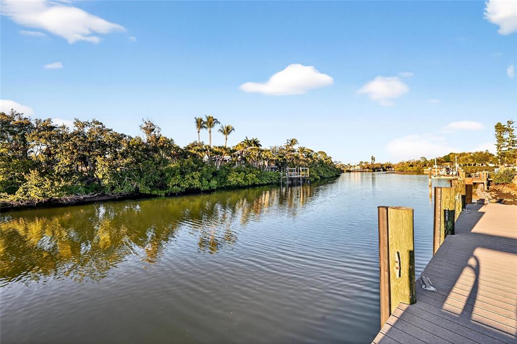A wooden dock overlooks a calm canal lined with lush trees and palm trees — 5424 AMERICA DRIVE, SARASOTA, FL