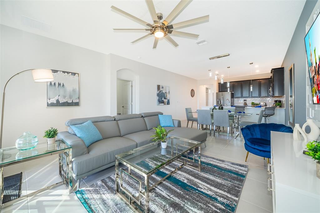 A modern open-concept living room features a grey sectional sofa, glass tables, and a kitchen — 9335 SOMMERSET HILLS DRIVE UNIT 9335, DAVENPORT, FL