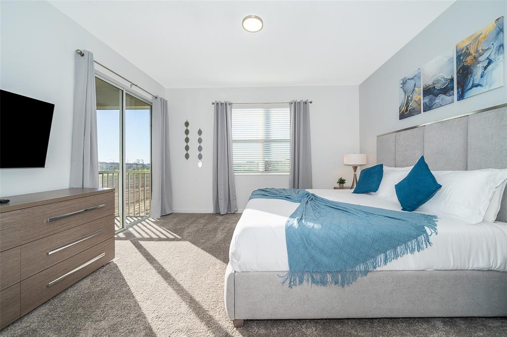 A bedroom features a gray upholstered bed, a dresser, and a sliding door to a balcony — 9335 SOMMERSET HILLS DRIVE UNIT 9335, DAVENPORT, FL