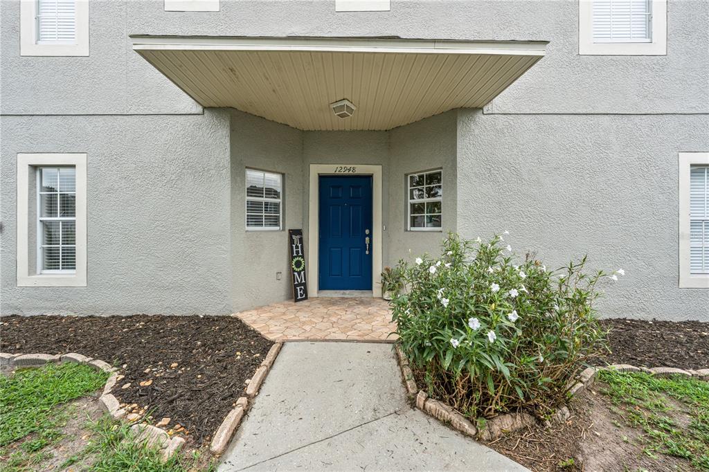 A blue front door is centered under a covered entryway on a gray stucco house — 12948 KINGS CROSSING DRIVE, GIBSONTON, FL