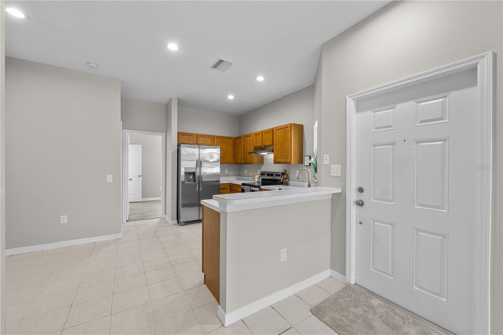 A kitchen with wooden cabinets, stainless steel appliances, and a breakfast bar near an entryway — 12948 KINGS CROSSING DRIVE, GIBSONTON, FL