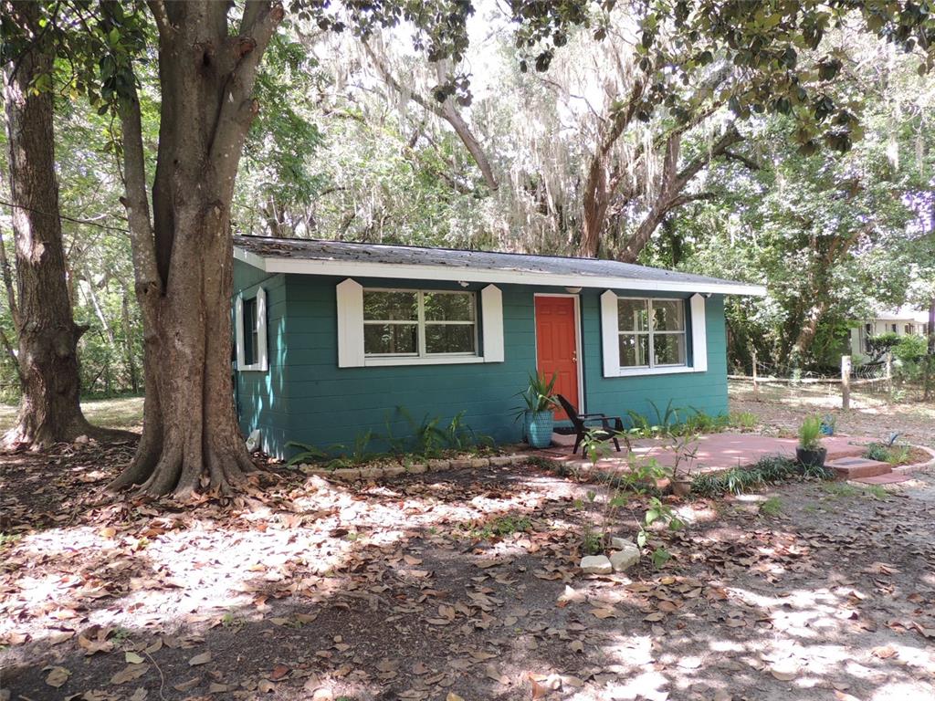 A teal-colored small house with a red door sits among trees on a dirt lot — 1146 NE 2ND PLACE, WILLISTON, FL