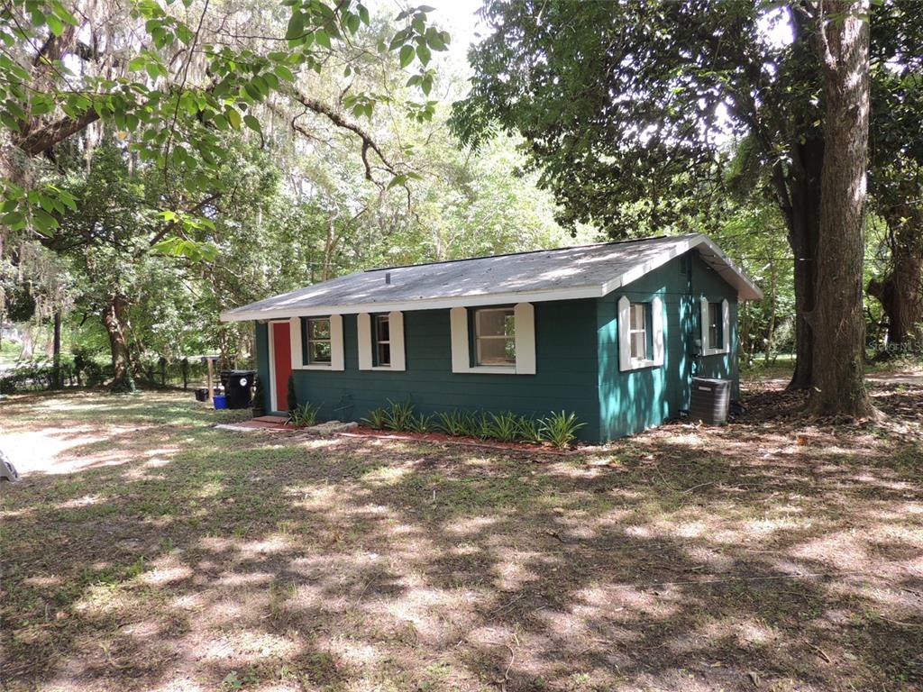 A small, dark green house with a red door sits in a wooded yard — 1146 NE 2ND PLACE, WILLISTON, FL