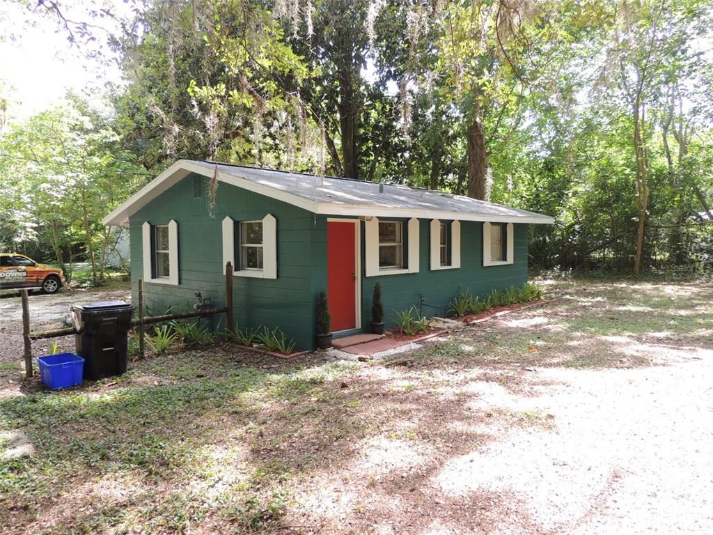 A small, green-painted house with a red front door sits on a wooded lot — 1146 NE 2ND PLACE, WILLISTON, FL