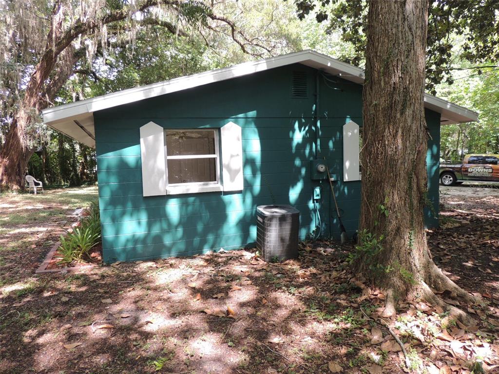 A teal-colored house exterior features a single window with white shutters and an AC unit — 1146 NE 2ND PLACE, WILLISTON, FL