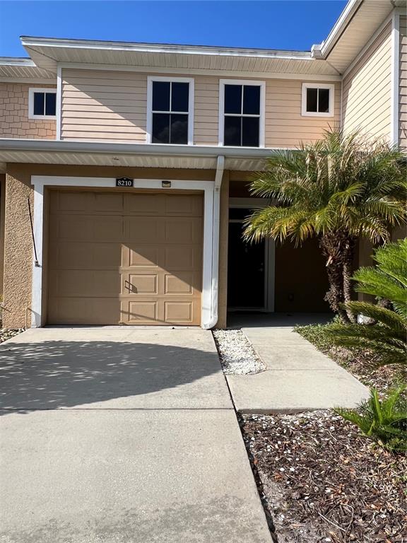 A two-story townhouse exterior features a tan garage door, a front entrance, and a palm tree — 8210 DOWN ROYAL ROAD, TAMPA, FL