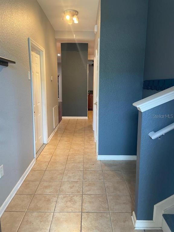 A hallway with tan tile flooring leads toward a dark accent wall and doorway — 8210 DOWN ROYAL ROAD, TAMPA, FL