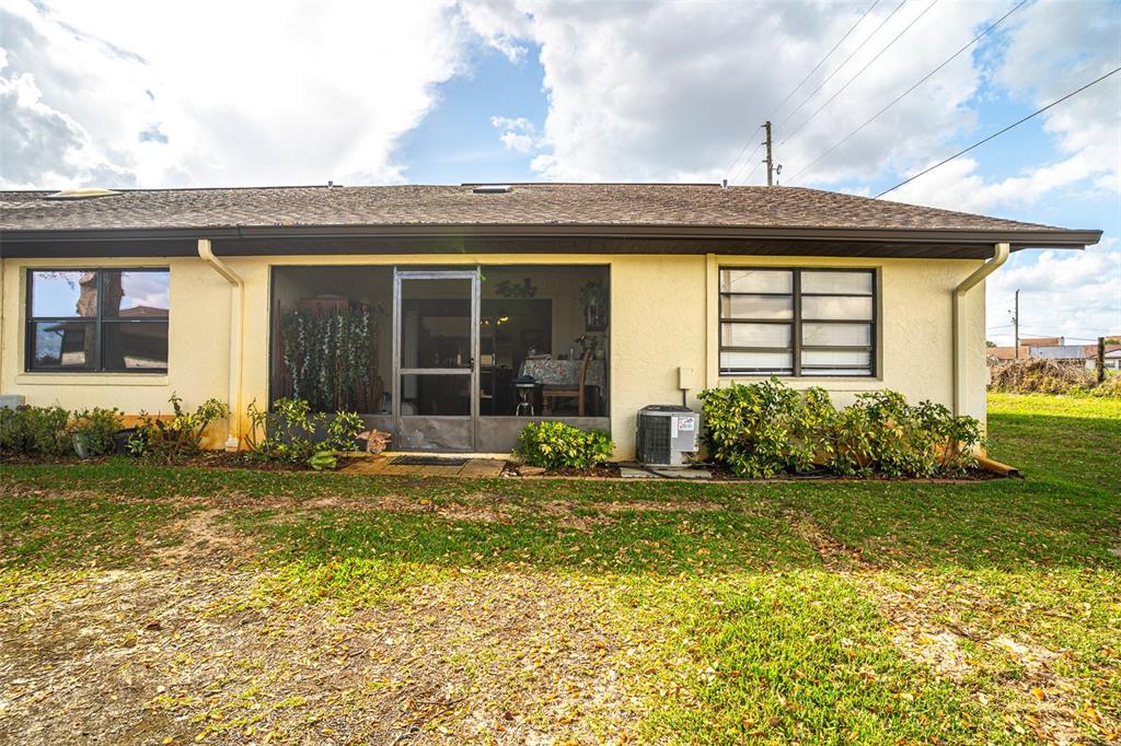 The exterior of a yellow house features a screened-in porch and an air conditioning unit — 15 CHARLTON DRIVE UNIT 15, LAKE PLACID, FL