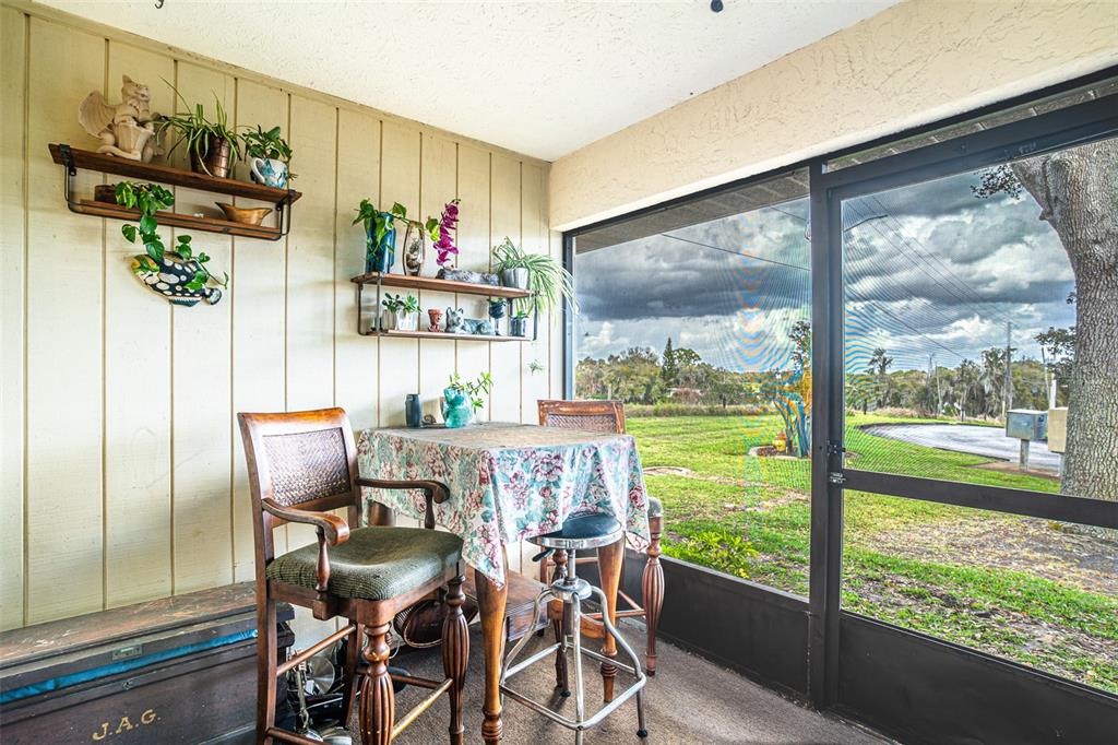 A screened-in porch features a small table, two chairs, wall-mounted shelving, and outdoor views — 15 CHARLTON DRIVE UNIT 15, LAKE PLACID, FL