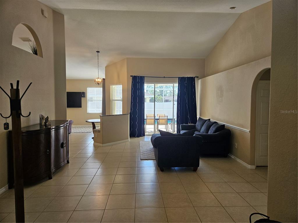 A living room with tile flooring, vaulted ceilings, dark furniture, and sliding glass patio doors — 779 NECTAR ROAD, VENICE, FL