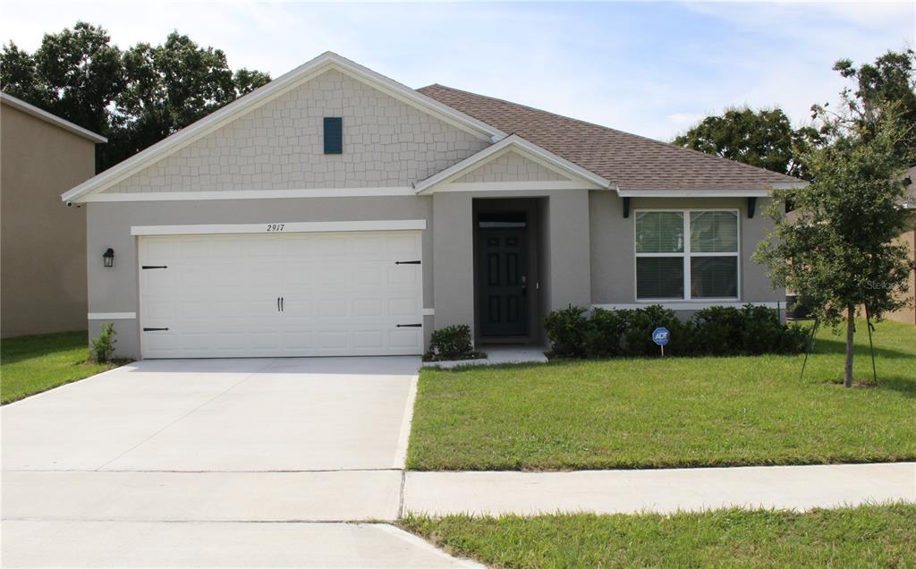 A single-story suburban house with a two-car garage, gray stucco siding, and shingled roof — 2917 CANARY LANE, TAVARES, FL