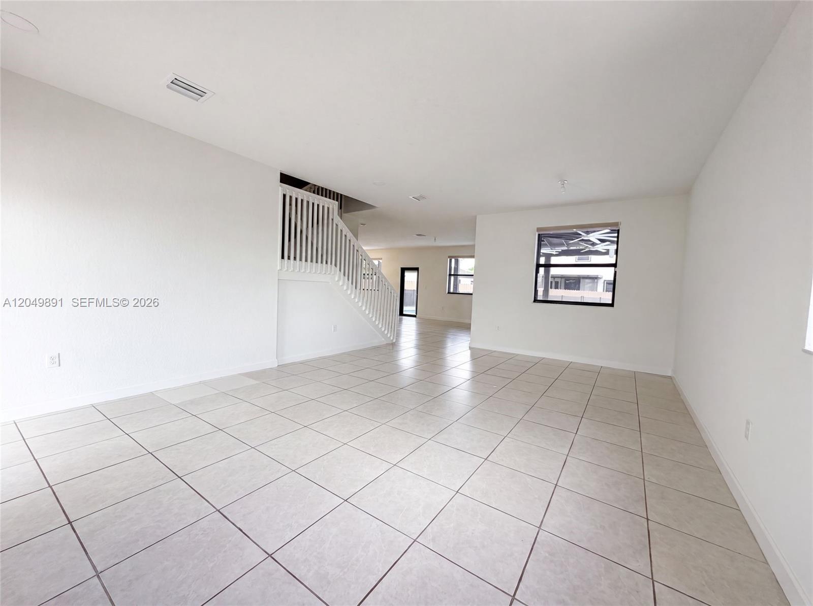An empty room features white walls, light-colored tile flooring, and a staircase with white railings — 12858 SW 228th St, Miami FL 33170, MIAMI, FL