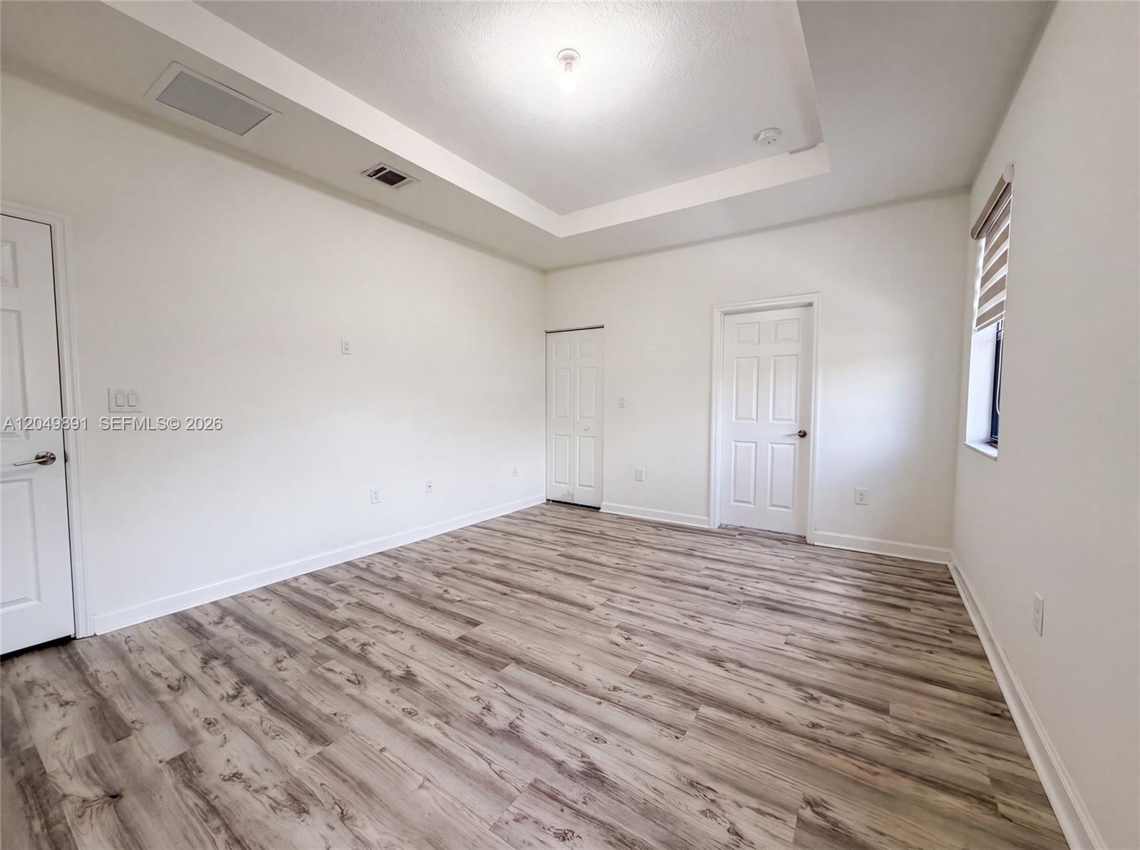 An empty bedroom features white walls, a tray ceiling, and light wood-look flooring — 12858 SW 228th St, Miami FL 33170, MIAMI, FL