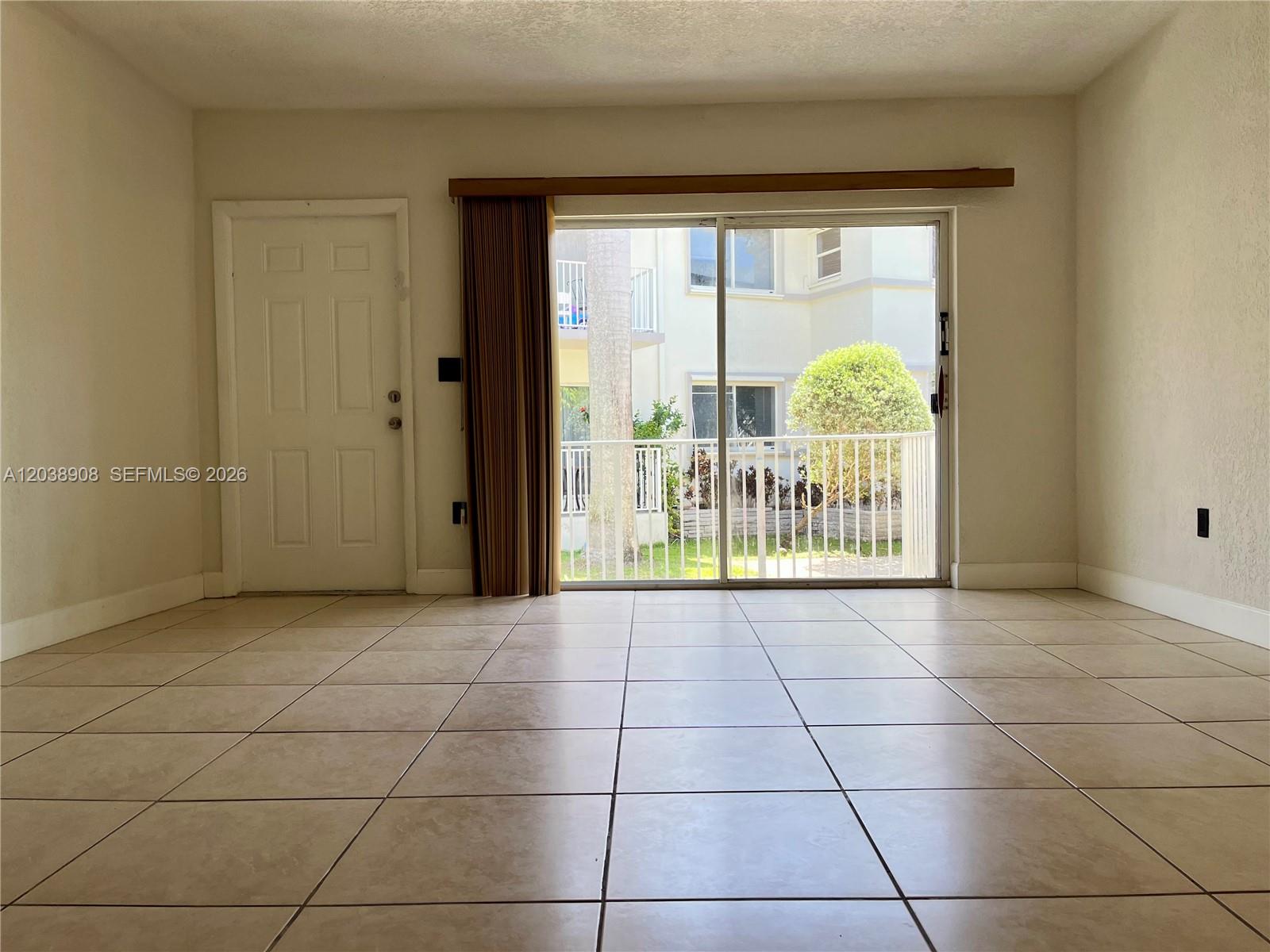 An empty room with beige tile flooring, a white door, and a sliding glass door — 1150 99th St # 6, Bay Harbor Islands FL 33154, BAY HARBOR ISLANDS, FL