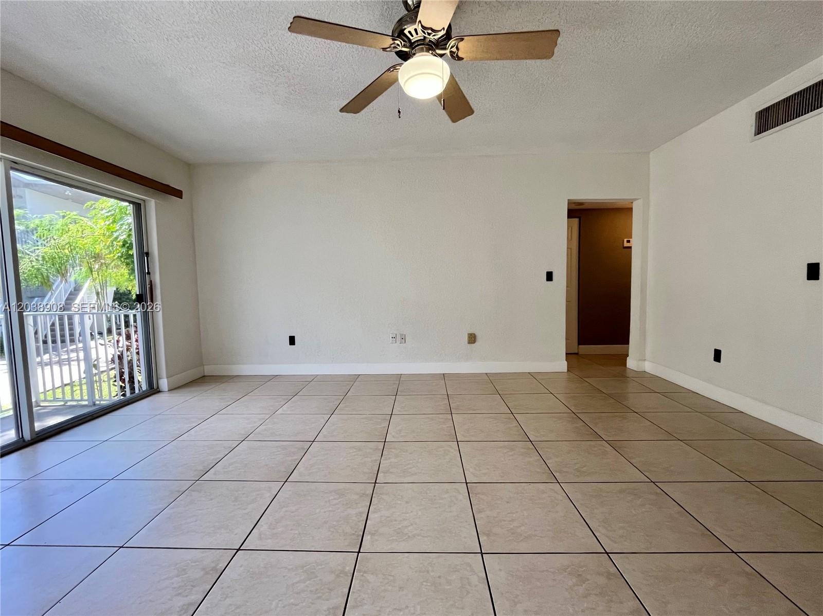 An empty room features beige tile flooring, white walls, a ceiling fan, and a sliding door — 1150 99th St # 6, Bay Harbor Islands FL 33154, BAY HARBOR ISLANDS, FL