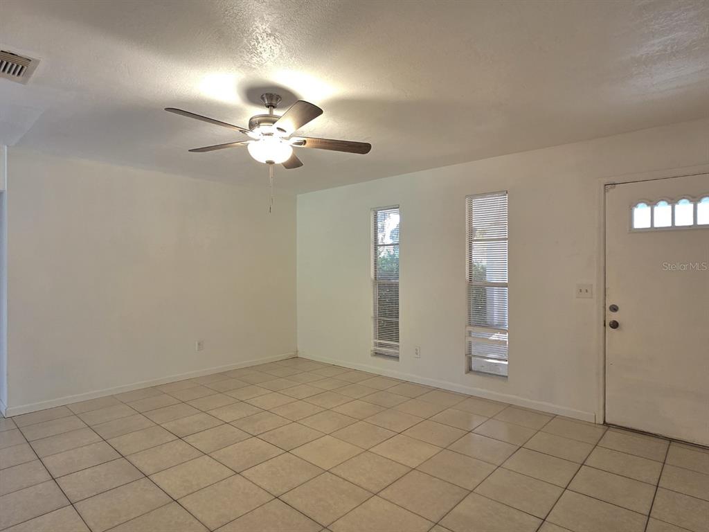 An empty room with light-colored tile flooring, a ceiling fan, and a white front door — 1537 MANGO TREE DRIVE, EDGEWATER, FL