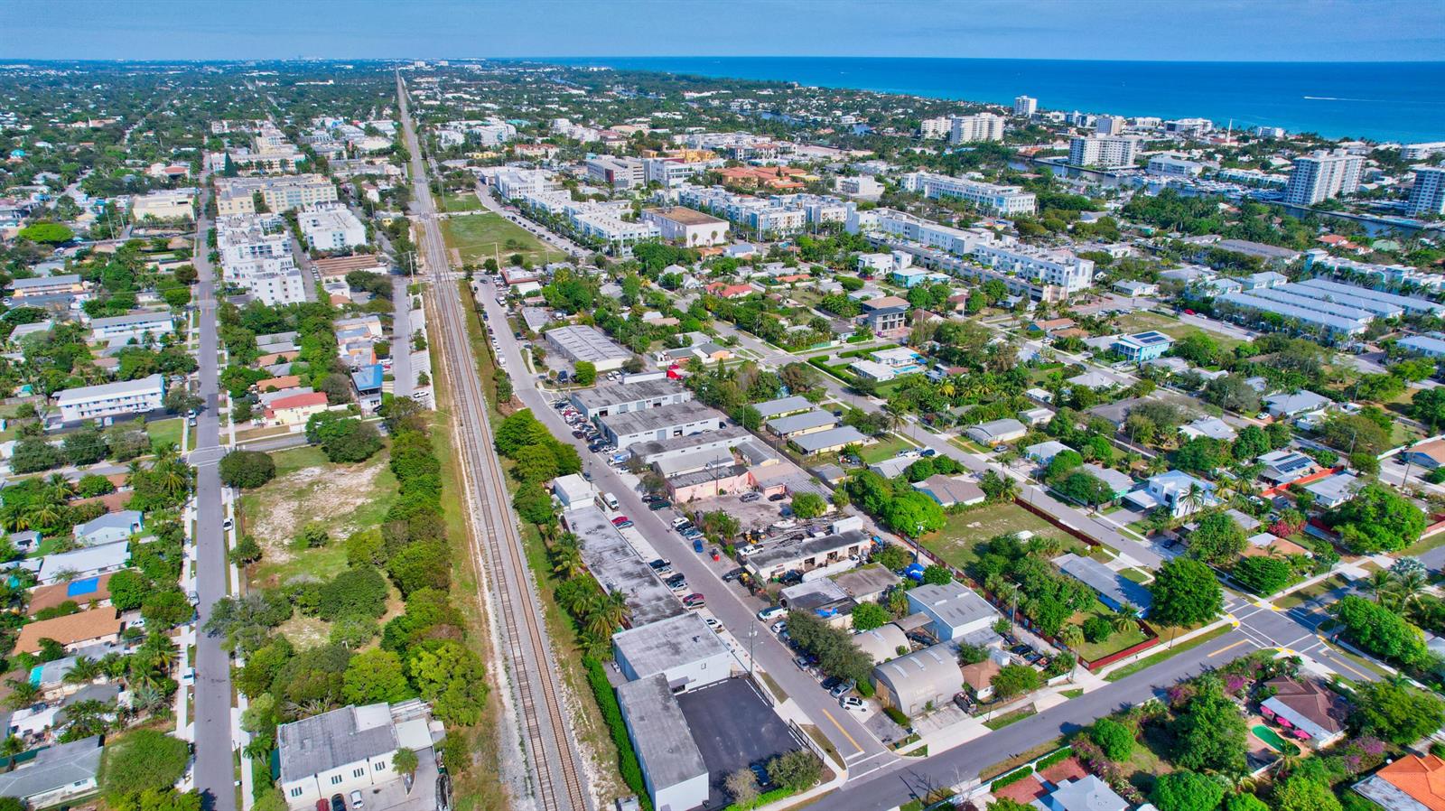 An aerial view shows a residential and industrial neighborhood bisected by a set of railroad tracks — 369 SE 2nd Avenue, Delray Beach FL 33483, DELRAY BEACH, FL