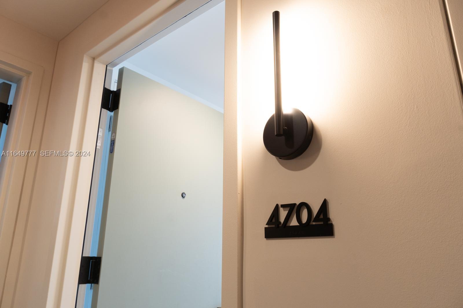 A modern wall sconce illuminates the number 4704 mounted next to an open doorway — 601 NE 1 Ave # 4704, Miami FL 33132, MIAMI, FL