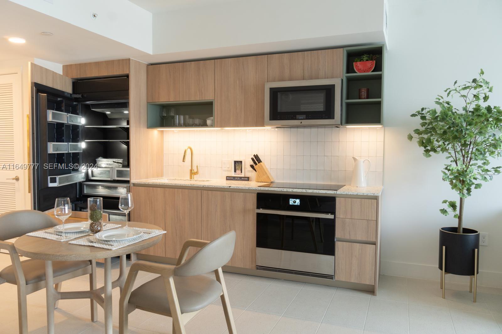 A modern kitchen features light wood cabinetry, gold fixtures, stainless steel appliances, and a dining area — 601 NE 1 Ave # 4704, Miami FL 33132, MIAMI, FL