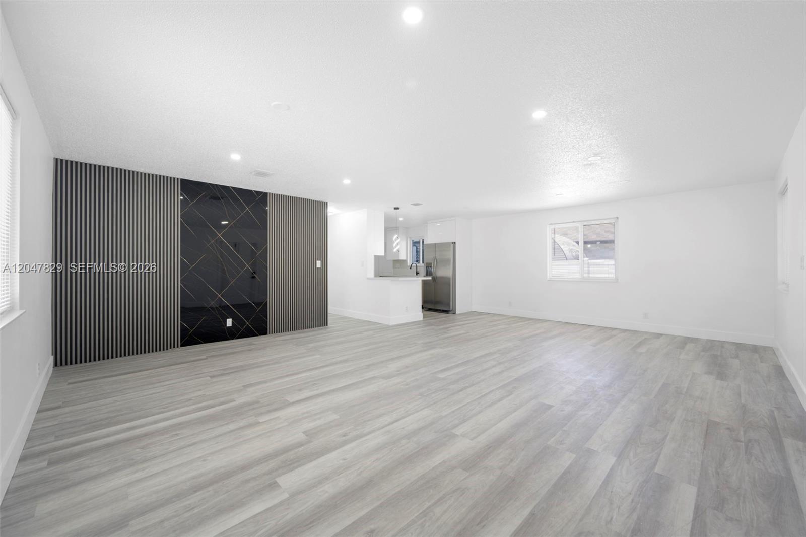 A living room features light wood-look flooring, white walls, and a black accent wall — 5580 Plunkett St, Hollywood FL 33021, HOLLYWOOD, FL