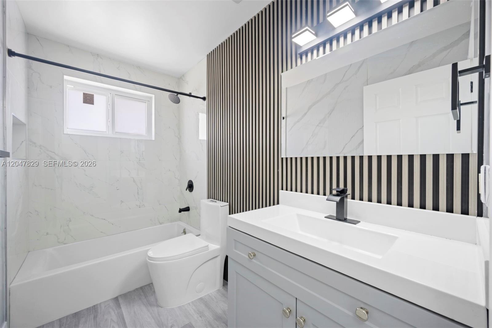 A bathroom features a white marble-tiled tub, a gray vanity, and a wood-slat accent wall — 5580 Plunkett St, Hollywood FL 33021, HOLLYWOOD, FL
