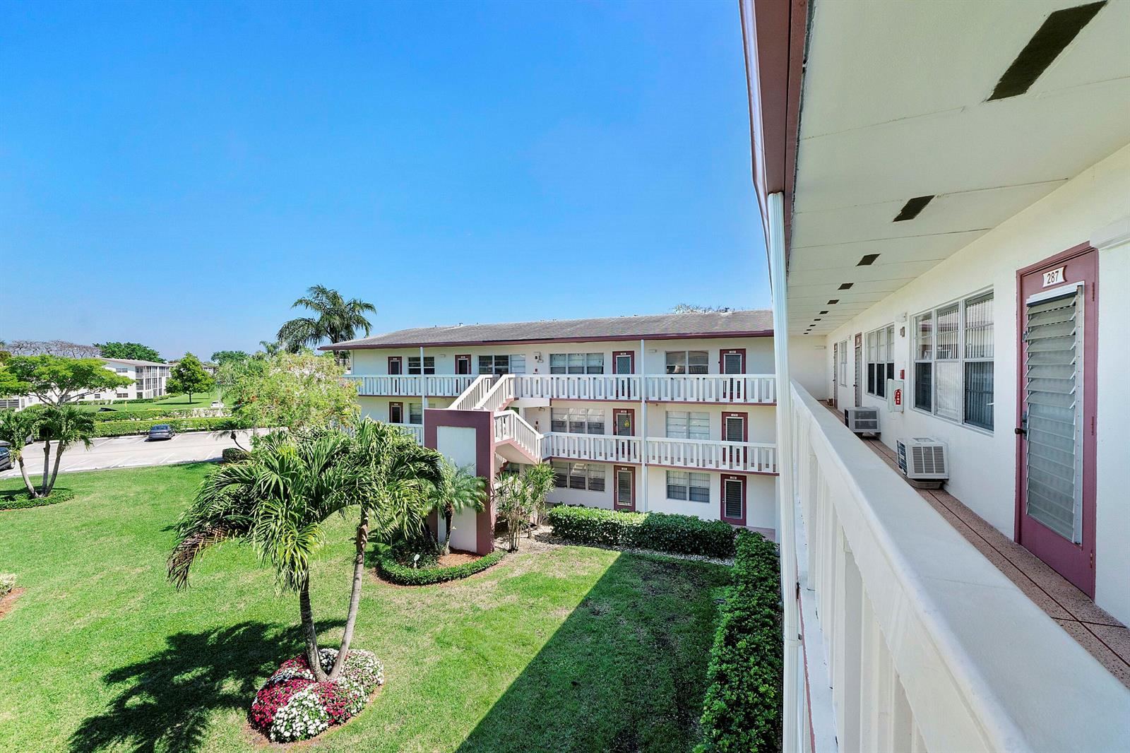 An exterior view of a multi-story apartment building with a balcony overlooking a grassy courtyard — 281 Fanshaw G, Boca Raton FL 33434, BOCA RATON, FL