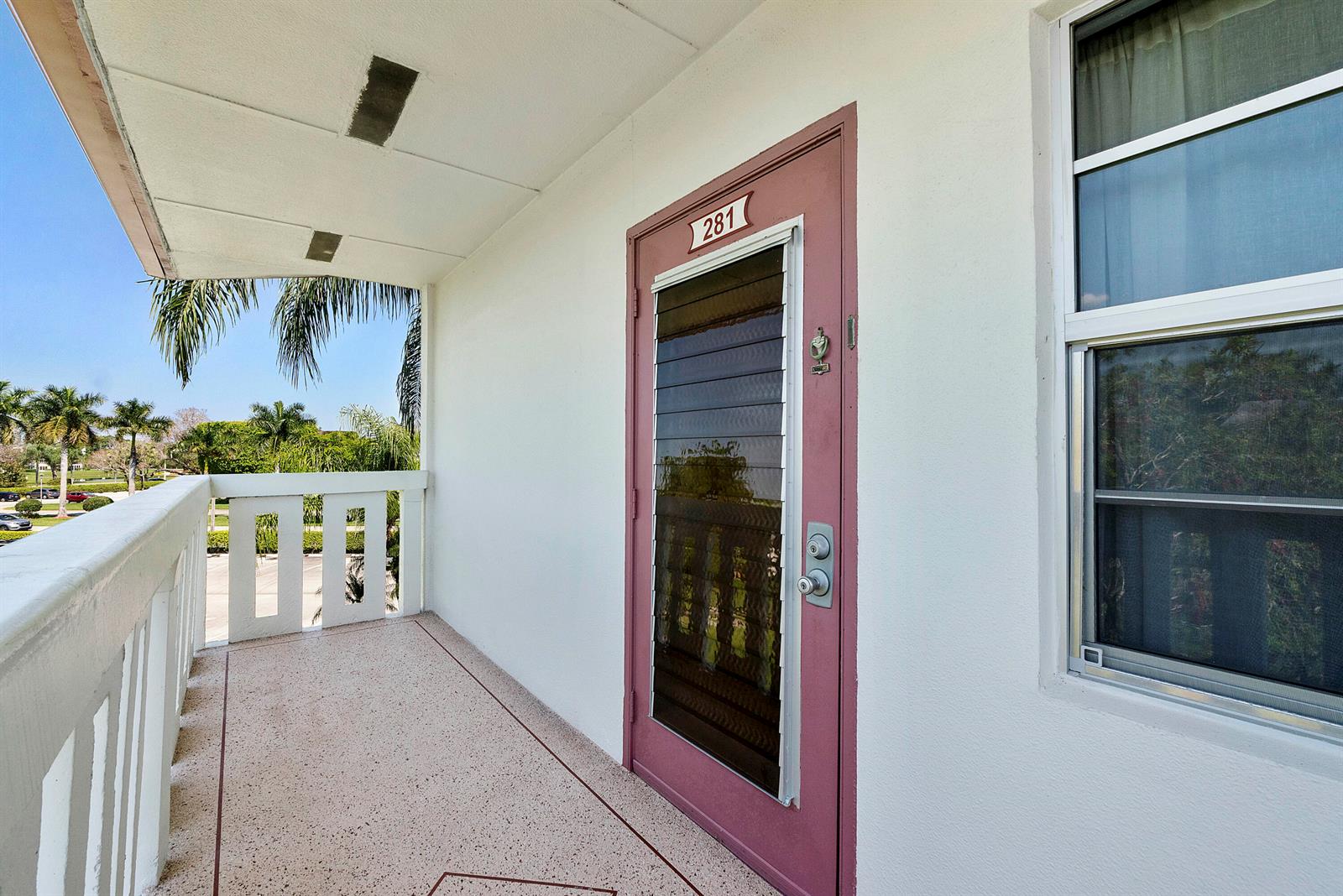 A balcony with a pink door numbered 281 and a white railing overlooks palm trees — 281 Fanshaw G, Boca Raton FL 33434, BOCA RATON, FL