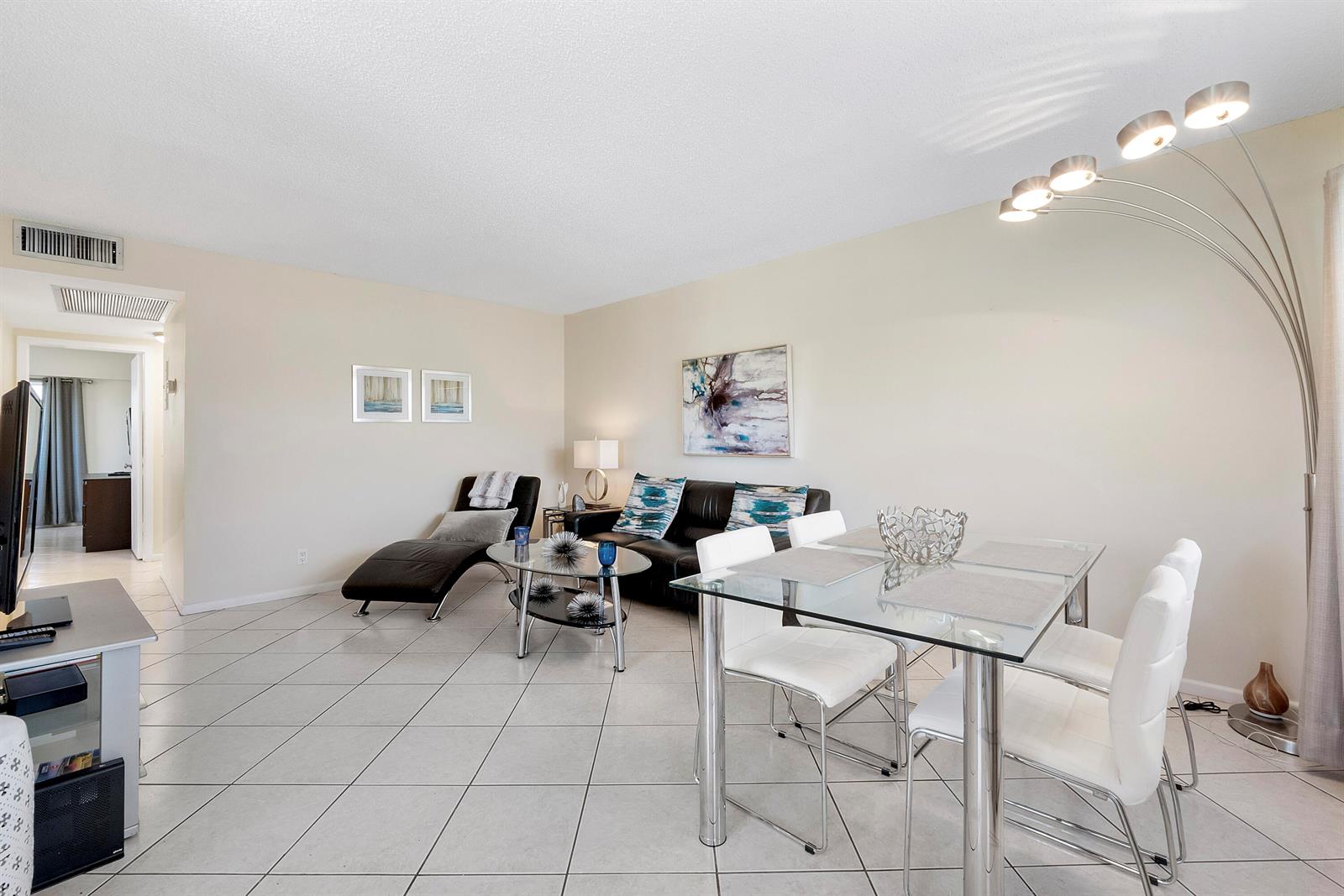A living and dining area features white tile floors, a glass table, and modern furniture — 281 Fanshaw G, Boca Raton FL 33434, BOCA RATON, FL