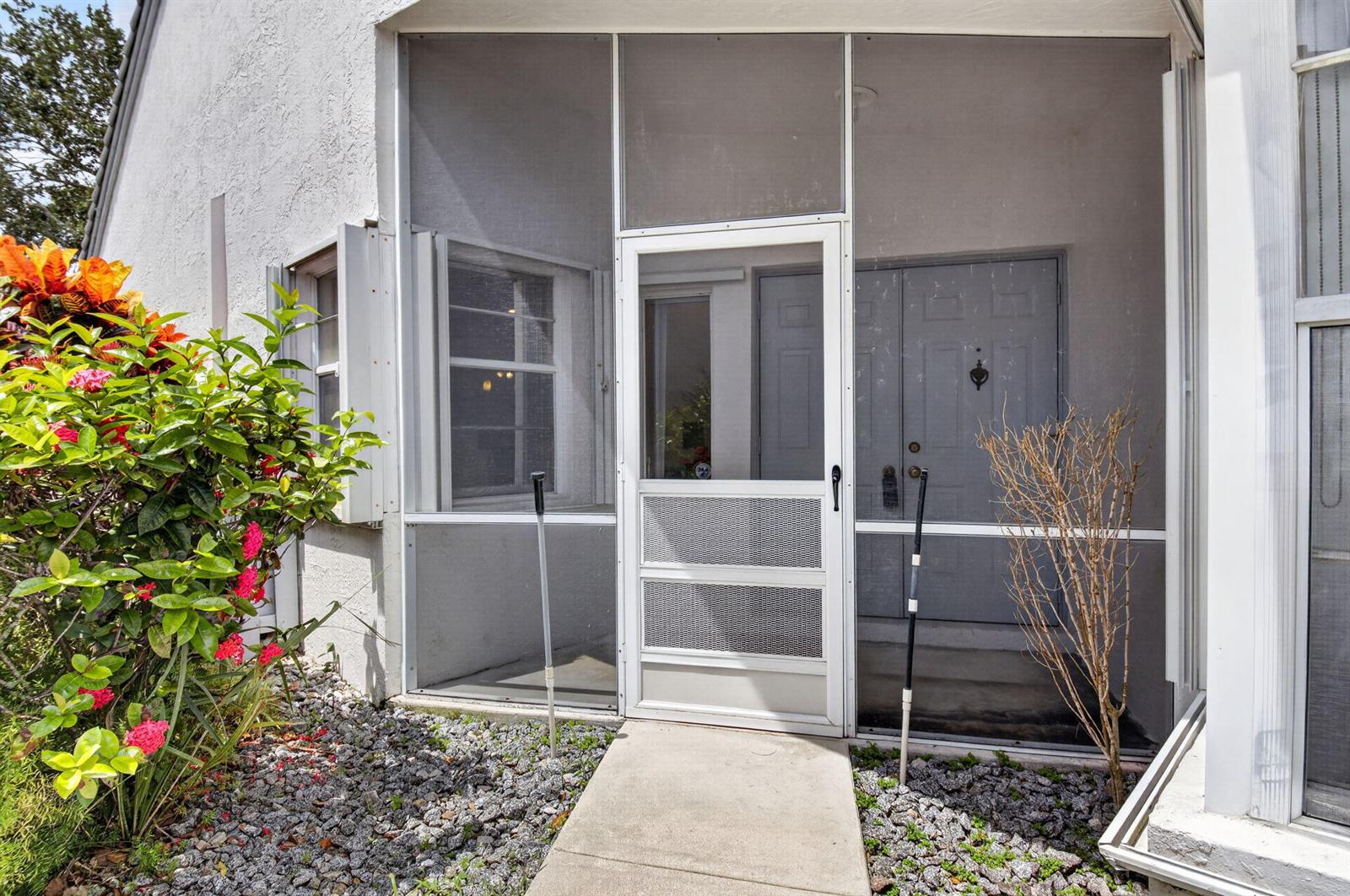 A concrete walkway leads to a screened-in front porch with a white door and siding — 10048 Country Brook Road, Boca Raton FL 33428, BOCA RATON, FL