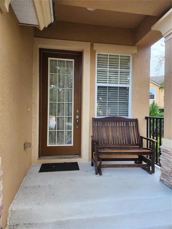 A covered front porch features a brown door, a window with blinds, and a wooden bench — 8119 VILLA GRANDE COURT, SARASOTA, FL