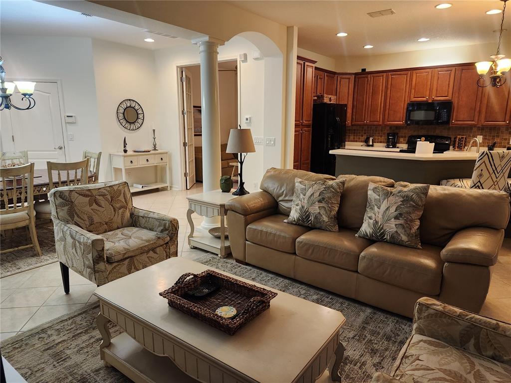 A living room with a leather sofa, patterned armchairs, and an open kitchen with wood cabinets — 8119 VILLA GRANDE COURT, SARASOTA, FL