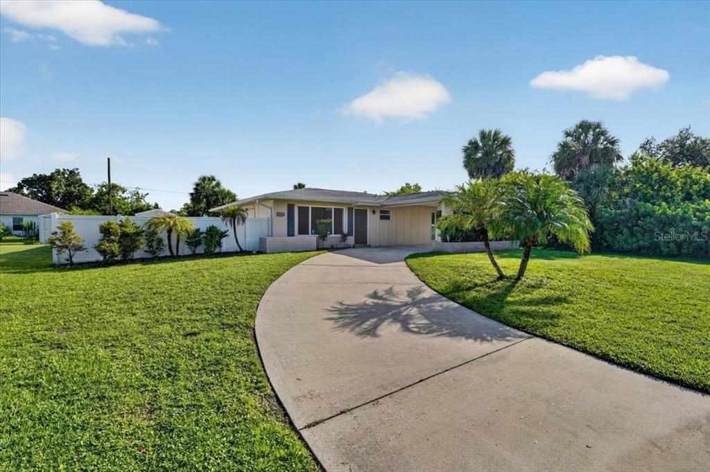 A single-story house with a curved driveway, lawn, and palm trees under a blue sky — 20286 BENTON AVENUE, PORT CHARLOTTE, FL