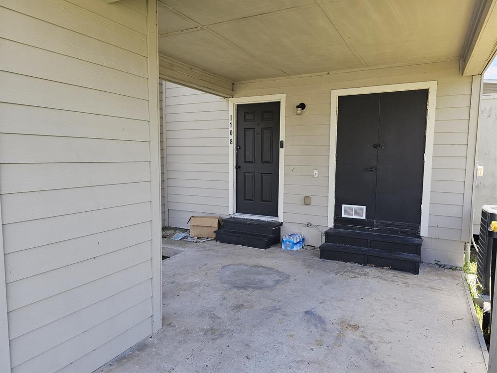A covered concrete patio features two black doors with small steps leading to each entrance — 1108 COUNTRY CLUB LANE, LAKELAND, FL