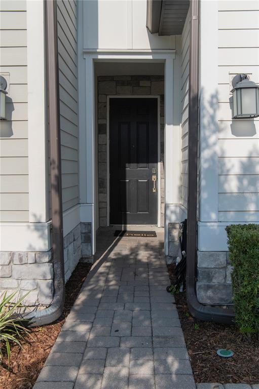 A stone-paved walkway leads to a black front door framed by light siding and stone — 11378 WHISTLING PINE WAY, ORLANDO, FL