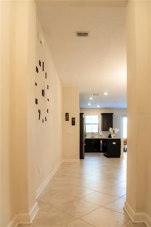 A hallway with a large wall clock leads into a kitchen with dark cabinetry — 11378 WHISTLING PINE WAY, ORLANDO, FL