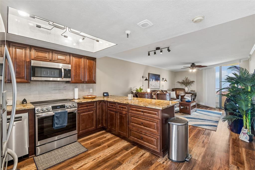 A kitchen with dark wood cabinets and granite countertops opens into a living area — 6009 SEA RANCH DRIVE UNIT 503, HUDSON, FL