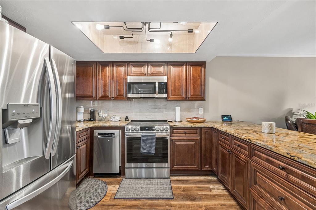 A kitchen with dark wood cabinets, granite countertops, stainless steel appliances, and a recessed ceiling light — 6009 SEA RANCH DRIVE UNIT 503, HUDSON, FL
